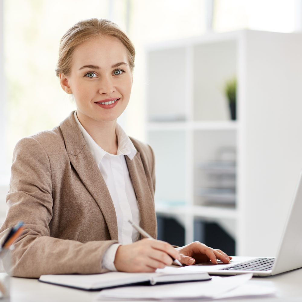 Pretty young accountant sitting by desk, planning work and browsing in the net